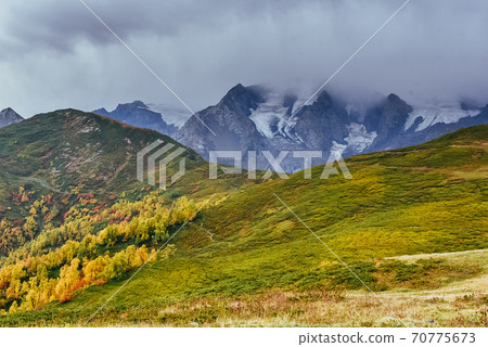 Autumn landscape and snowy mountain peaks. Birch forest in sunlight. Main Caucasian Ridge. Mountain View from Mount Ushba Mheyer, Georgia 70775673