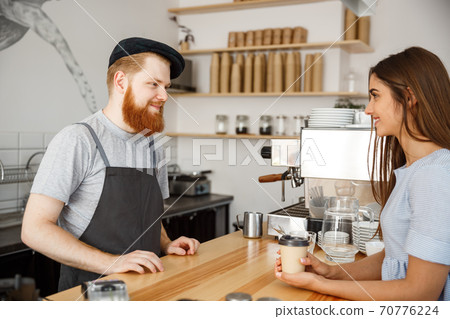 Coffee Business Concept - young beared handsome barista talking with beautiful caucasian customer in modern coffee shop. 70776224