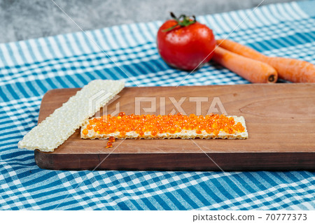 Crackers with red caviar on a wooden board with tomato, carrots and a tablecloth 70777373