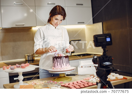 Confectioner in a uniform decorates the cake Confectioner in a uniform decorates the cake 70777675