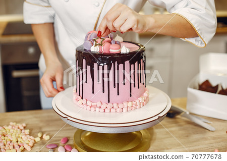 Confectioner in a uniform decorates the cake 70777678