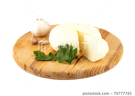 Round soft cheese, parsley leaf and garlic on a wooden cutting board. 70777785