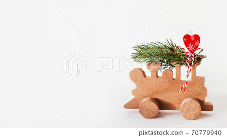 Wooden train with tied fir tree branches and red heart decoration. Cute symbol of Christmas tree brought home for New Year celebration. Winter holiday spirit. Copy space on white background. Wooden train with tied fir tree branches and red heart decoration. Cute symbol of Christmas tree brought home for New Year celebration. Winter holiday spirit. Copy space on white background. 70779940