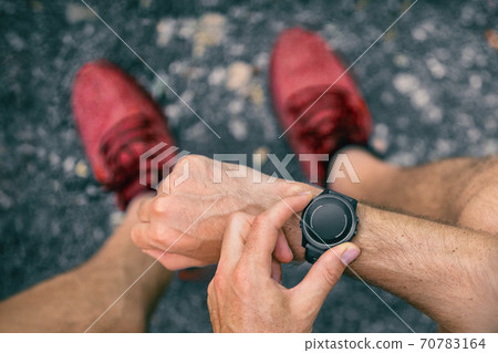 Smartwatch wearable tech device fit athlete man checking smart sport watch technology on fitness run jog outside. First person view from above showing red running shoes Smartwatch wearable tech device fit athlete man checking smart sport watch technology on fitness run jog outside. First person view from above showing red running shoes 70783164