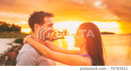 Happy couple in love embracing at sunset glow on Florida beach summer vacation background. Asian woman with arms around neck of caucasian boyfriend. Horizontal crop 70783921