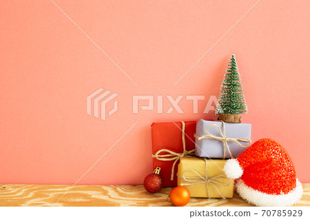 Christmas concept. Gift boxes with fir tree, baubles, santa claus hat on wooden table with coral pink background 70785929