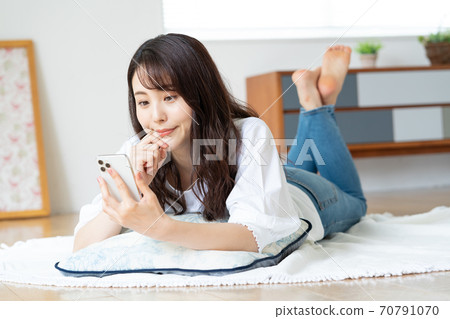 Smiling young woman lying on the living room and looking at the smartphone 70791070