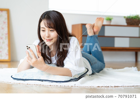 說謊在客廳和看智能手機的微笑的少婦 70791071