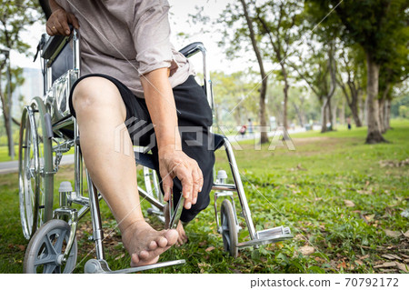 Asian senior woman hand hold nail clippers in wheelchair, female elderly people cutter her toenails or pedicure, trying to reach or bend down to trimmer the nails with difficulty, lifestyle concept 70792172