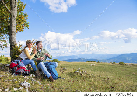 Young couple drinking water while resting on the rock during the travel in the mountains Young couple drinking water while resting on the rock during the travel in the mountains 70793642