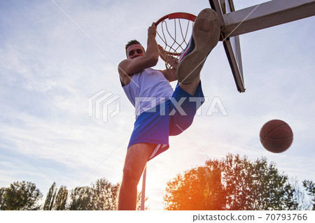 Young man jumping and making a fantastic slam dunk playing streetball, basketball. Urban authentic. 70793766