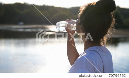 Girl quench their thirst on a hot sunny day after a jog, drink water. Healthy lifestyle.Woman in the Open air Drinks Water from a Bottle Girl quench their thirst on a hot sunny day after a jog, drink water. Healthy lifestyle.Woman in the Open air Drinks Water from a Bottle 70794562