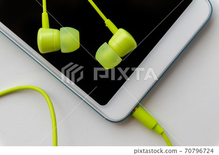 Modern smartphone with lime headphones on light background. Closeup, selective focus 70796724