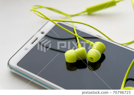 Modern smartphone with lime headphones on light background. Closeup, selective focus 70796725