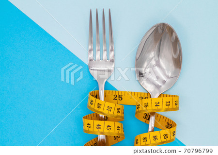 Fork and spoon is strung by a ribbon for measuring on a colored background. Symbol of diet and weight loss Fork and spoon is strung by a ribbon for measuring on a colored background. Symbol of diet and weight loss 70796799