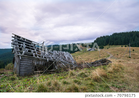 Ruined building in the middle of mountain, surrounded by spruce trees with the cloudy sky above. 70798175