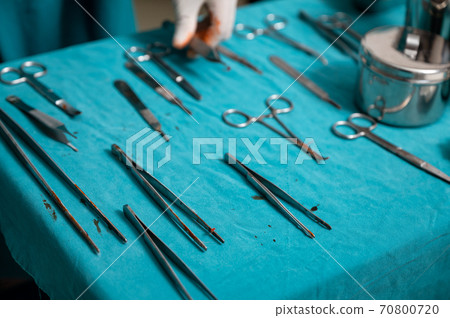 Surgeon hand wear medical gloves choosing surgical instruments on a table in operating room Surgeon hand wear medical gloves choosing surgical instruments on a table in operating room 70800720