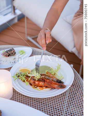 Woman hand using fork dipping grilled shrimp seafood on white plate at restaurant Woman hand using fork dipping grilled shrimp seafood on white plate at restaurant 70800745