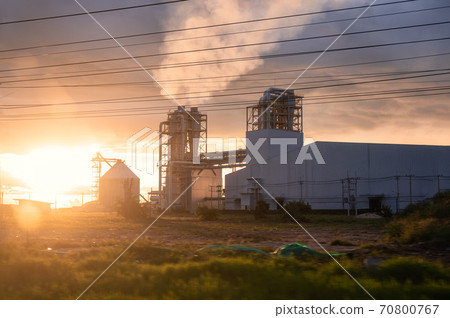 Sunset over Industrial pipe building of fiberboard factory working with release smoke from chimney 70800767