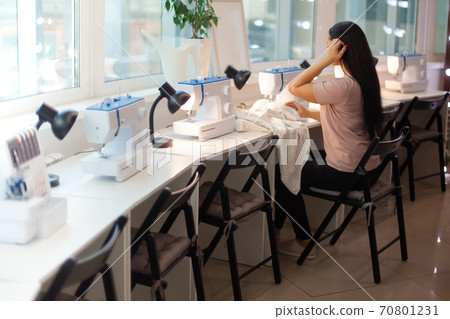 Beautiful woman tailor with long dark hair completing work with sewing machine at workplace 70801231