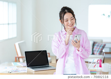 Telework A smiling young woman operating a smartphone in the living room 70802118