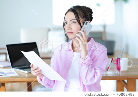 Telework A young woman with a troubled face talking on a smartphone with documents in her hand in the living room 70802492