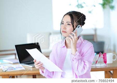 遠程辦公一名年輕女子在客廳裡談電話與文檔的智能手機 遠程辦公一名年輕女子在客廳裡談電話與文檔的智能手機 70802494