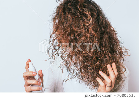 Woman applying moisturizing spray to her curly Woman applying moisturizing spray to her curly 70803533