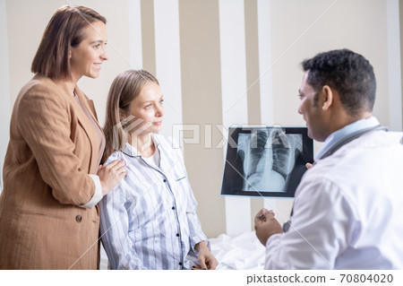 Confident radiologist with lung x-ray looking at his patient and her friend Confident radiologist with lung x-ray looking at his patient and her friend 70804020