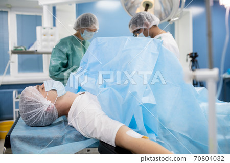 Young male patient in protective mask and headwear lying on operation table 70804082