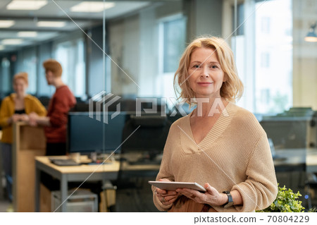 Mature blond businesswoman in casualwear using tablet in front of camera 70804229