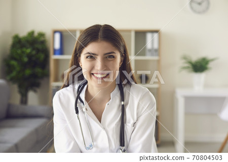 Smiling woman doctor therapist sitting and looking at camera in medical clinic office Smiling woman doctor therapist sitting and looking at camera in medical clinic office 70804503
