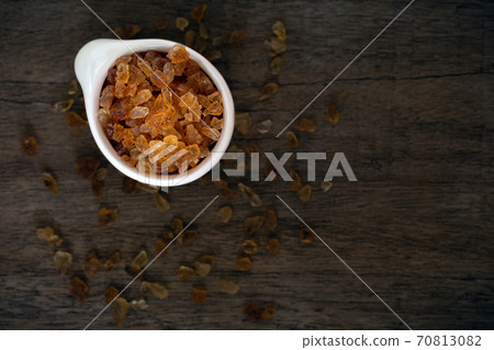 Natural organic brown crystal rock sugar in white ceramic cup over old wooden background. 70813082