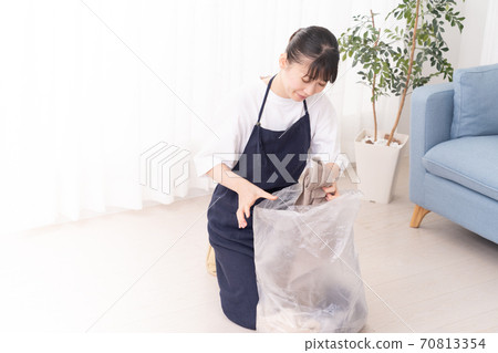 Young woman putting thrown clothes in a trash bag 70813354