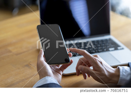 Man with smartphone in front of laptop 70816751