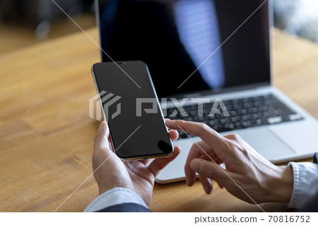 Man with smartphone in front of laptop 70816752