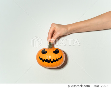 Hand holds halloween pumpkin on white wall Hand holds halloween pumpkin on white wall 70817028