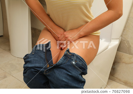 Woman holding groin sitting on toilet bowl 70827098