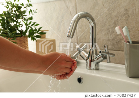 Woman washing hands under the water tap in sink 70827427