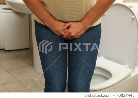 Woman holding groin in bathroom near toilet bowl 70827443