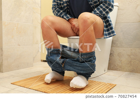 A man sits with his pants down on the toilet A man sits with his pants down on the toilet 70827454