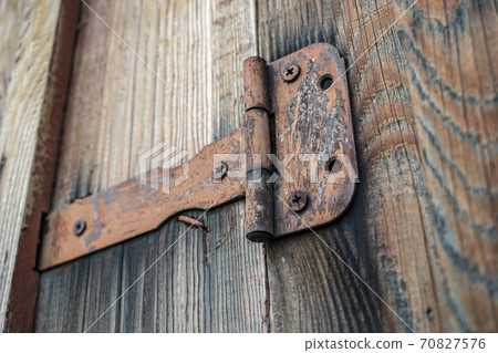 Old and rusty door hinge holding a wooden gate closed Old and rusty door hinge holding a wooden gate closed 70827576