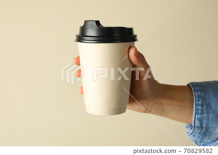 Female hand hold paper cup of coffee on beige background 70829582