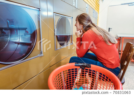 Woman waits on chair in front of washing machine Woman waits on chair in front of washing machine 70831063
