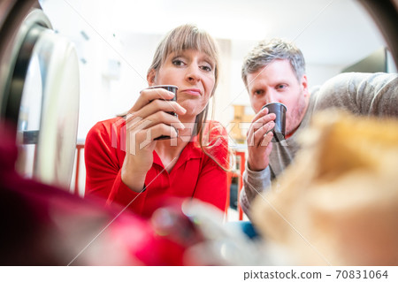 Couple looks into washing machine with coffee cup 70831064