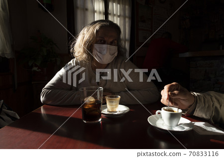 A woman, wearing a mask, watches sitting at a bar table, Spain A woman, wearing a mask, watches sitting at a bar table, Spain 70833116