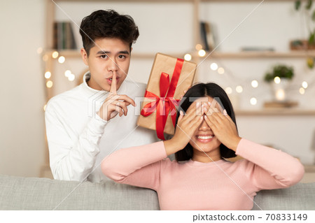 Asian Husband Holding Wrapped Gift Making Surprise For Wife Indoor 70833149