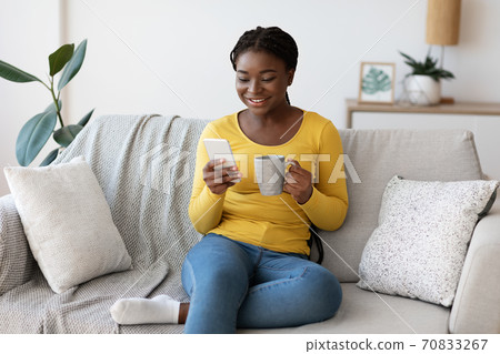 Domestic Relax. Positive black lady resting on couch with smartphone and coffee Domestic Relax. Positive black lady resting on couch with smartphone and coffee 70833267