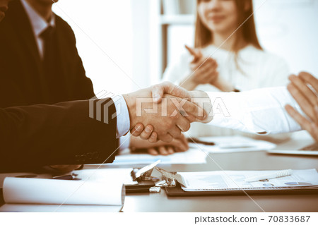 Business people shaking hands at meeting while theirs colleagues clapping and applauding. Group of unknown businessmen and women in modern white office. Success teamwork, partnership and handshake Business people shaking hands at meeting while theirs colleagues clapping and applauding. Group of unknown businessmen and women in modern white office. Success teamwork, partnership and handshake 70833687