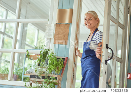 Middle aged woman holding handle on garden house door Middle aged woman holding handle on garden house door 70833886